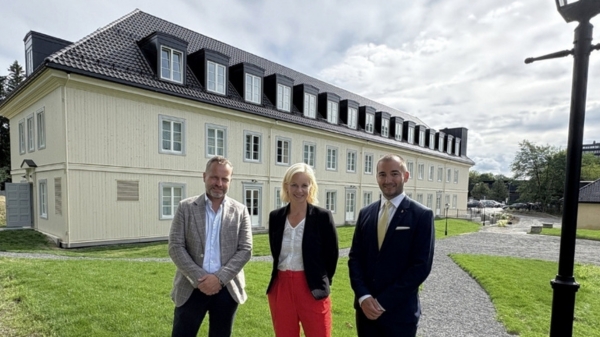 Tre personer fremfor hybelbygg av tremoduler på grønt gress.