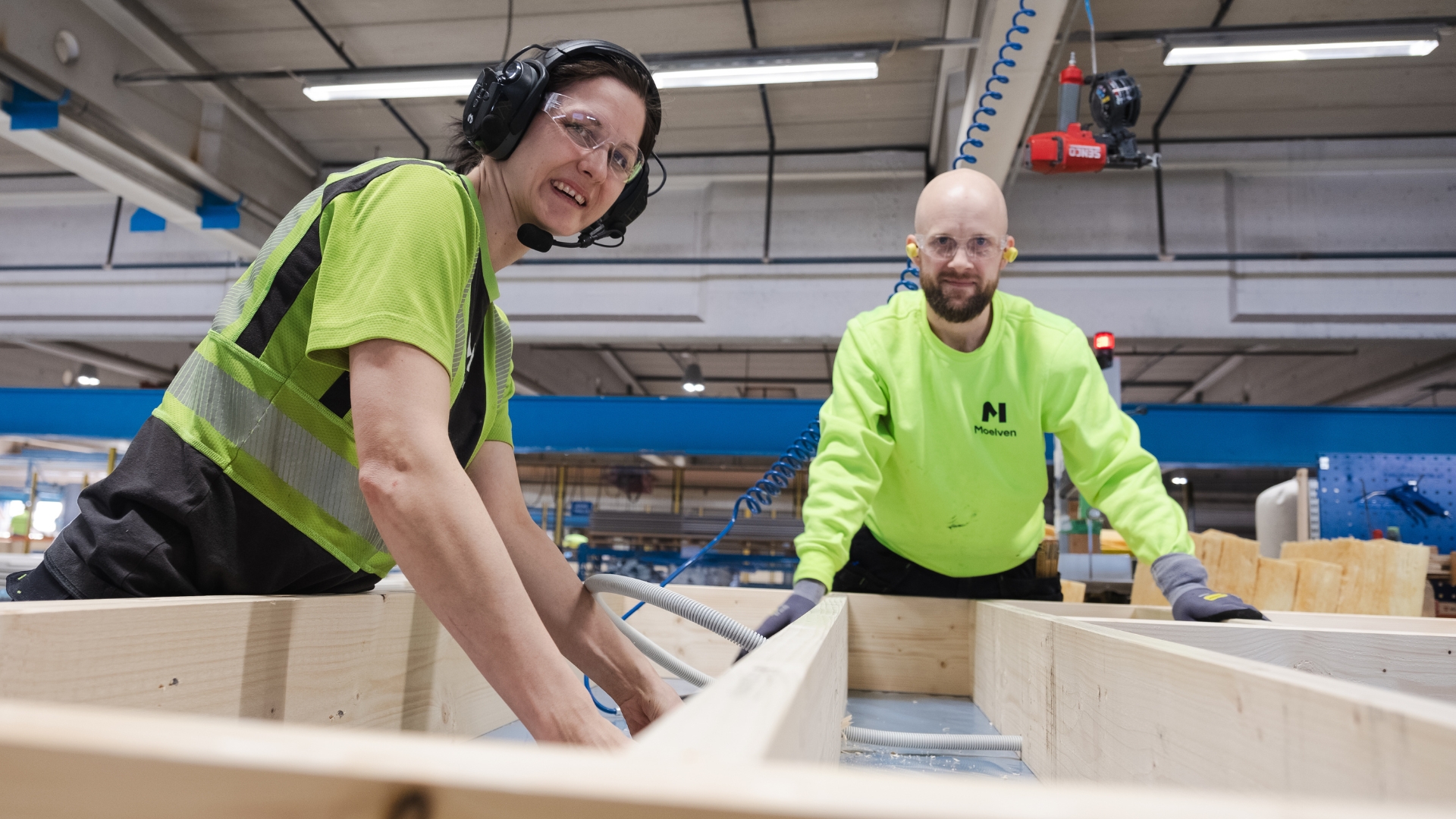 Kvinne og mann som bygger rammen til et gulvelement i fabrikk.