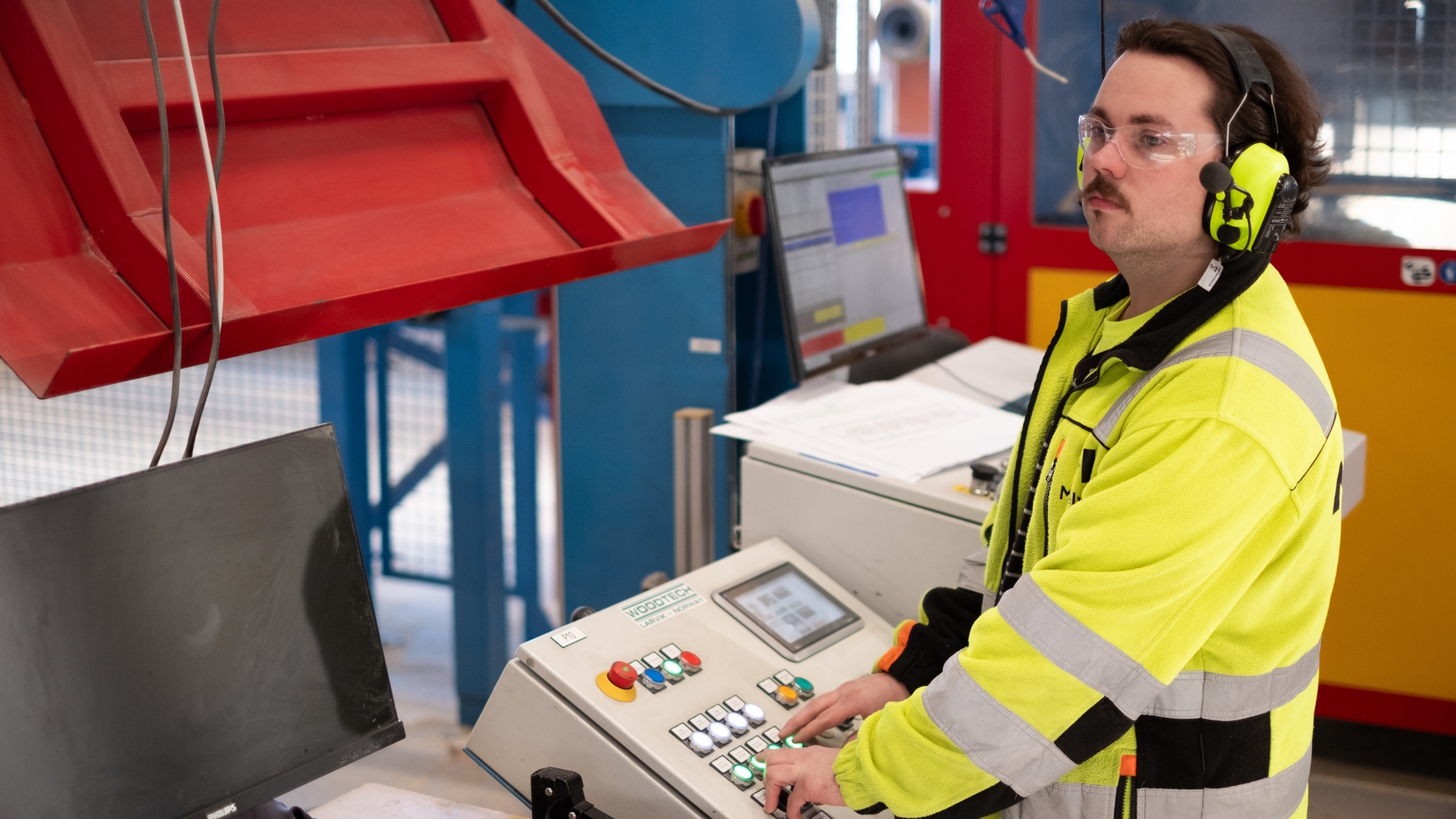 Fabrikkarbeider med hørselvern som styrer CNC-maskiner.
