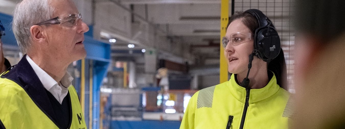 To personer i synlighetstøy snakker sammen io fabrikklokale.
