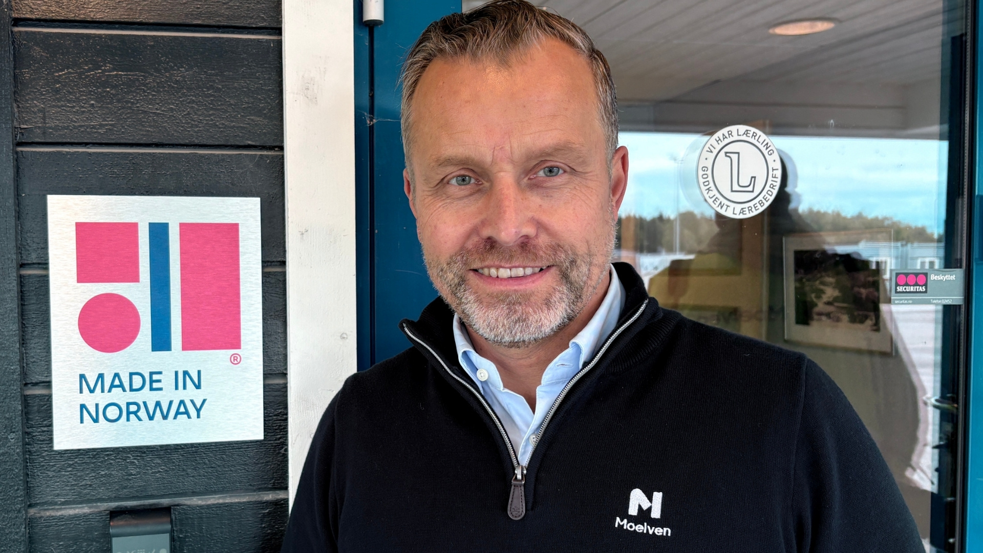 Smilende mann i Moelven-genser står ved siden av et Made in Norway-skilt
