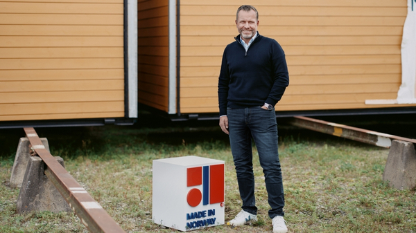 Moelven-ansatt står utenfor en tremodul og har en Made in Norway-kube på bakken.
