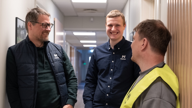 Drei lächelnde Moelven-Kollegen stehen in einem Korridor.