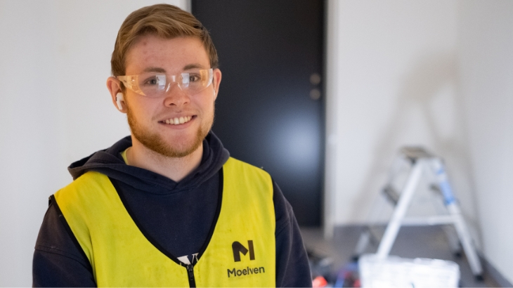 Ung, smilende person med Moelven refleksvest og beskyttelsesbriller.