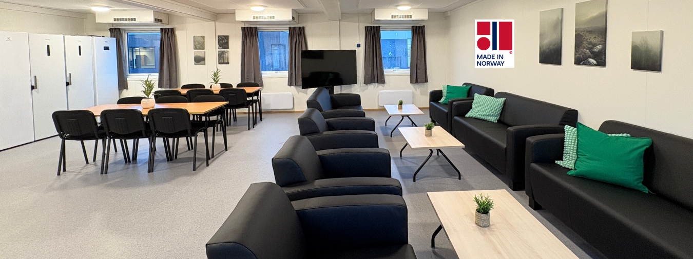 Lyst og moderne fællesrum i modulbyggeri med sofaer, borde og spisepladser.