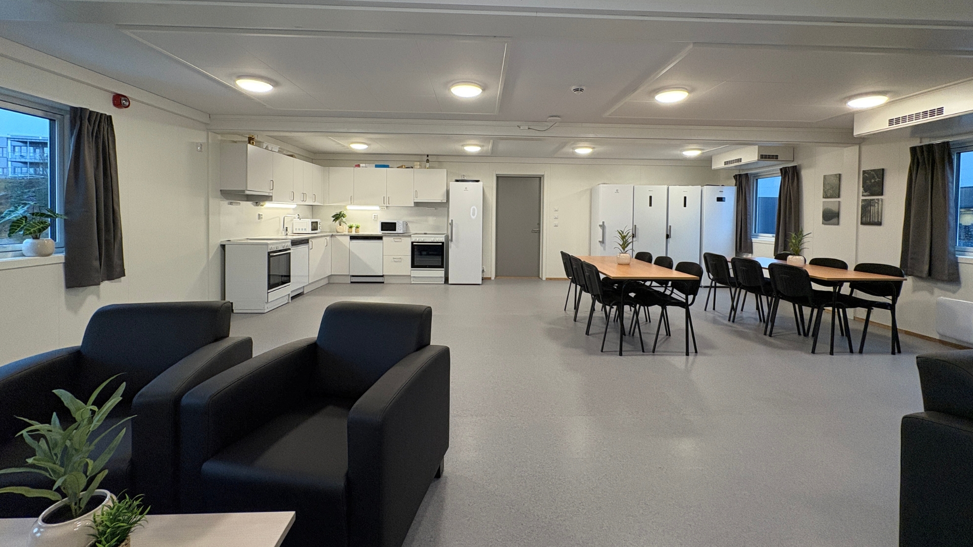 Fælles opholdsrum i boligpavillon med fuldt udstyret køkken, spiseborde og plads til socialisering