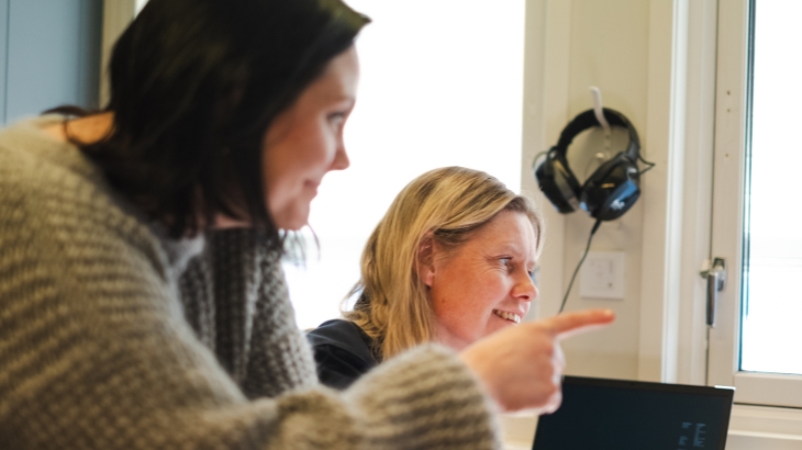 Two smiling colleagues looking at the same thing. One of them is pointing.