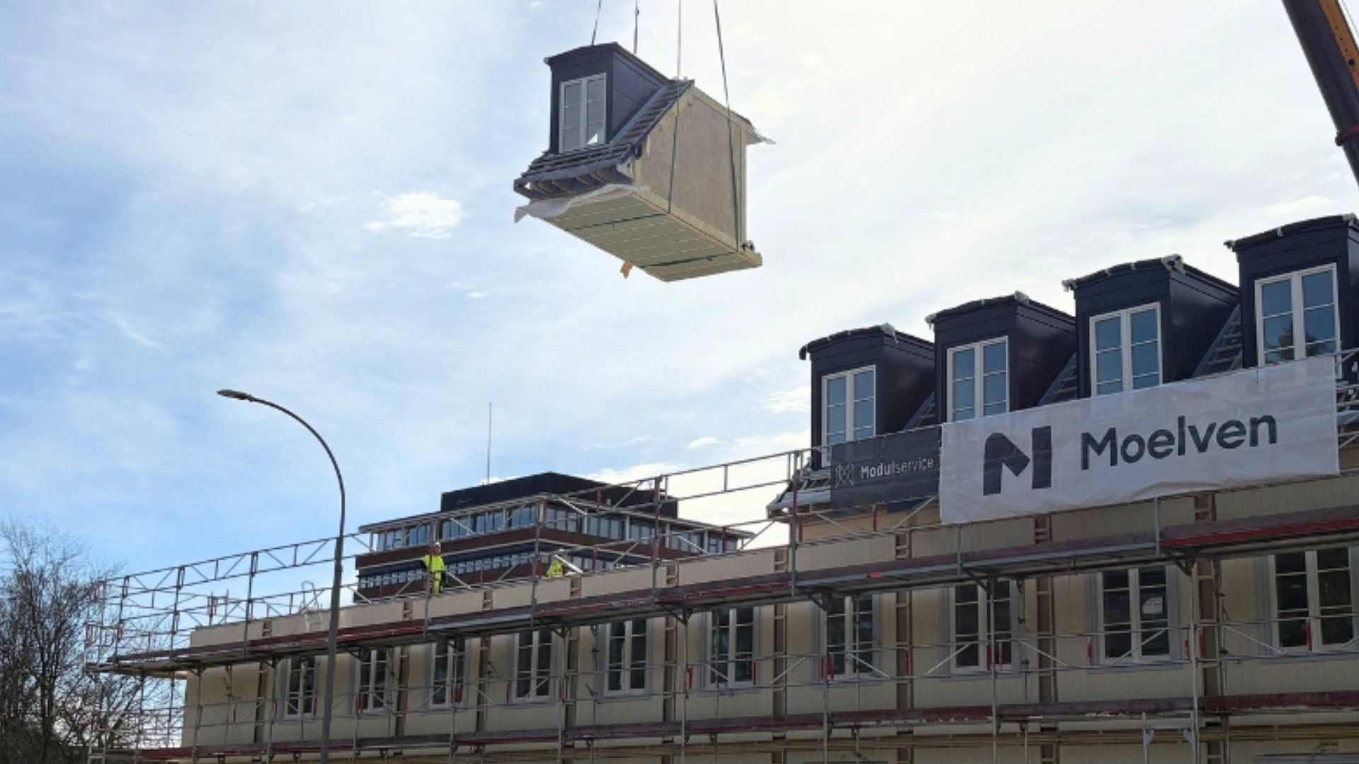 Viðareining sem hangir í loftinu í krana yfir einingabyggingu.