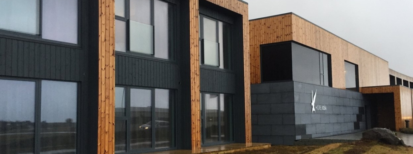 Tveggja hæða einingahús með stórum gluggum, ljósbrúnni og svörtum viðarklæðningu.