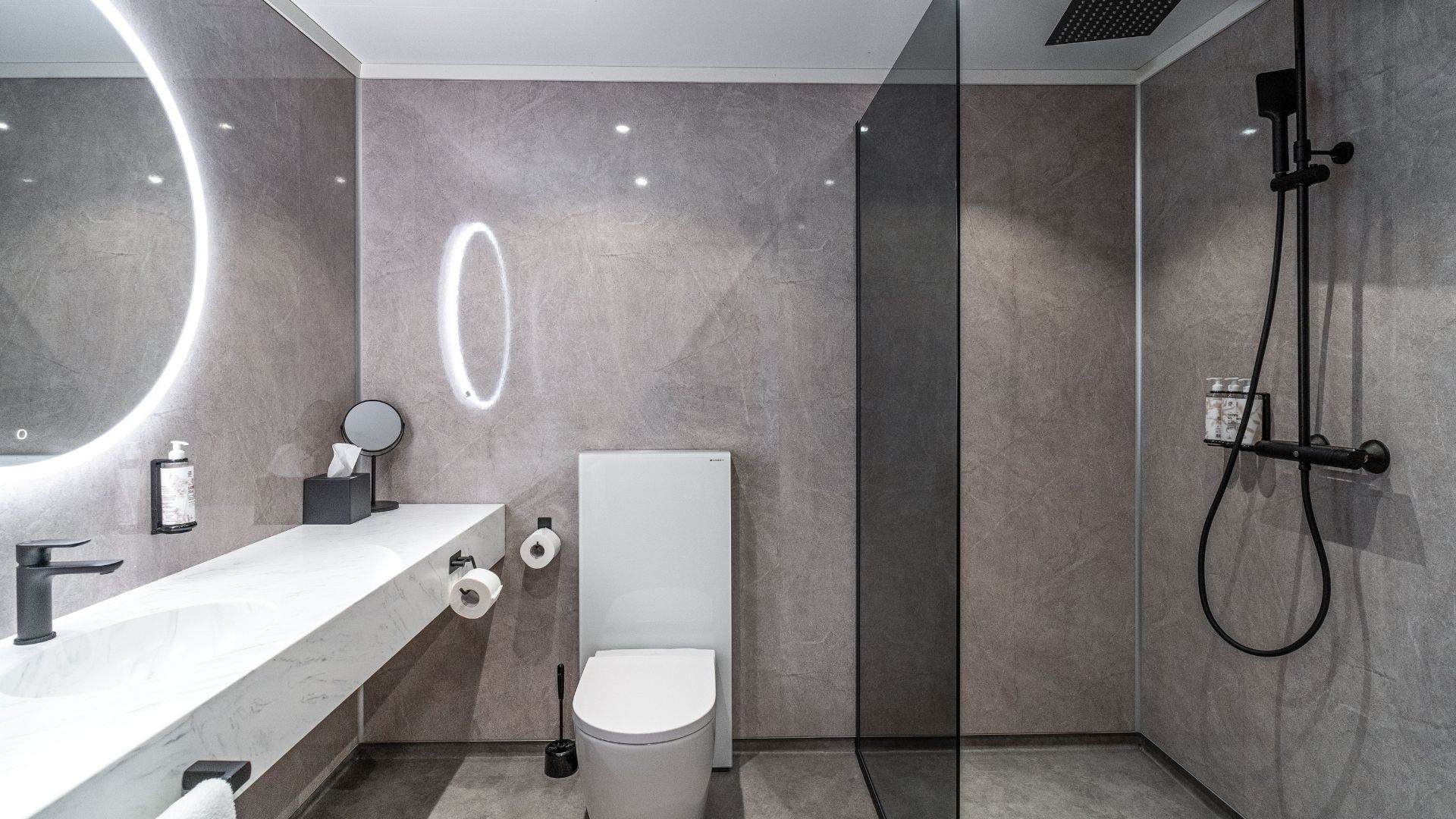 Nútímalegt baðherbergi á hóteli með sturtu, spegli og upphengdu salerni.