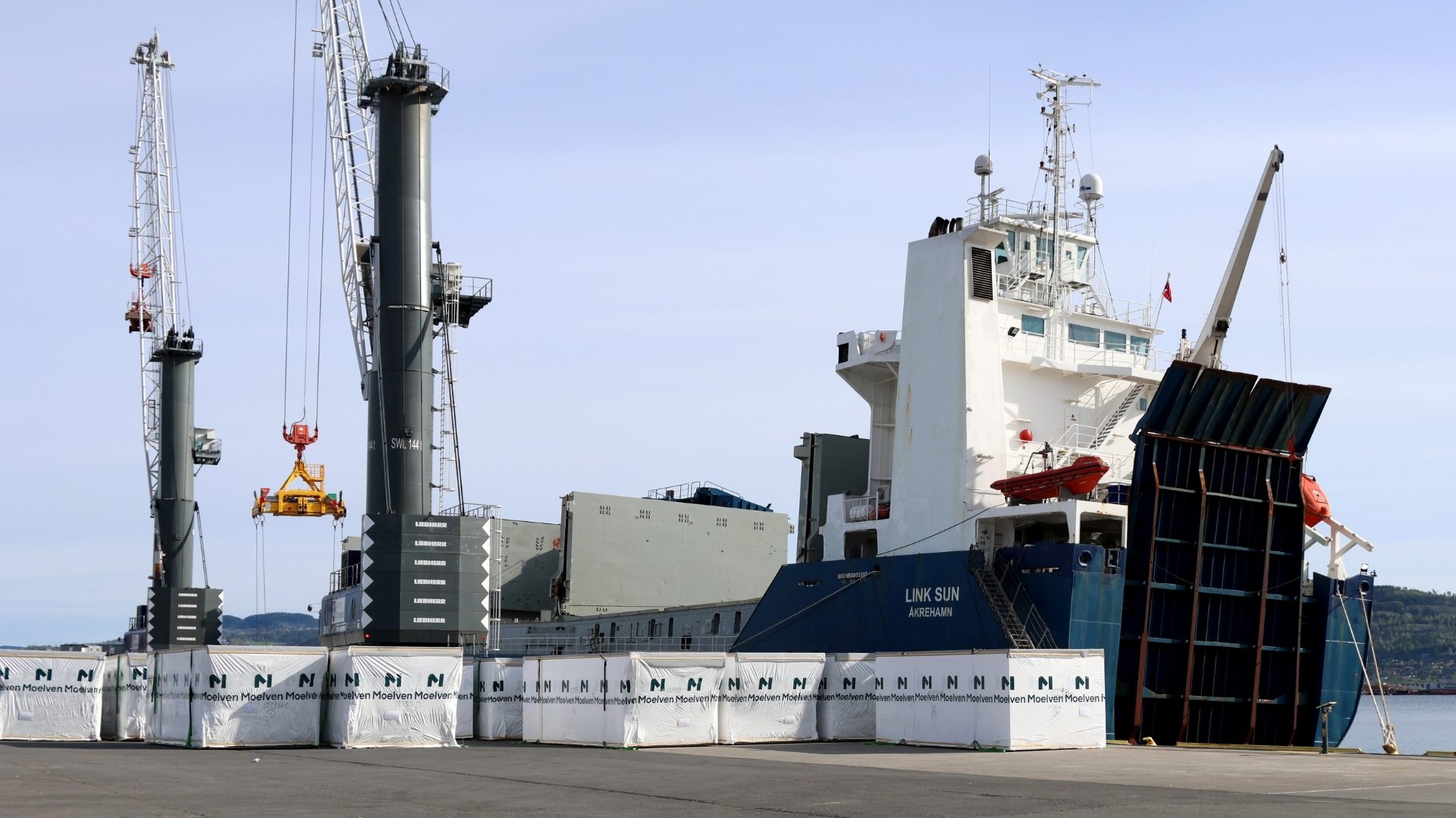 Flutningaskip við höfn þar sem einingar til byggingarframkvæmda eru hífðar um borð.