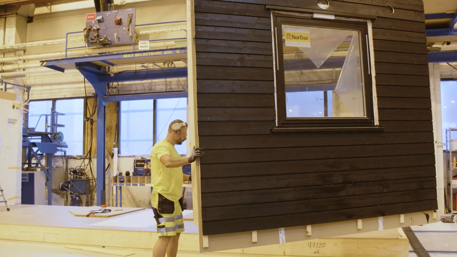 Робітник фабрики тримає стіновий елемент, що висить на крані.