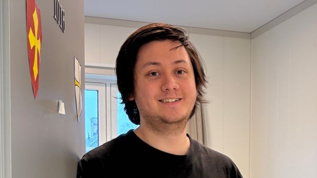 Smilende person som står i døråpningen inn til hybelen sin.