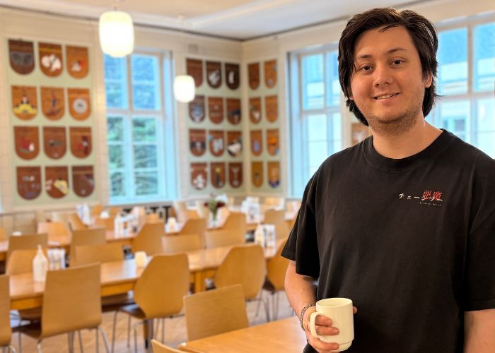 Person som holder en kaffekopp og står i en sal med masse skjold på veggene.