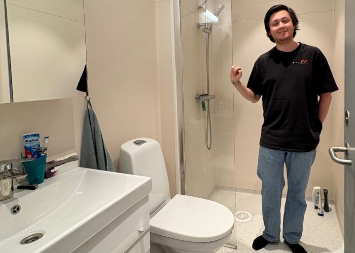 Person står på et lite bad med dusj, toalett og vask.