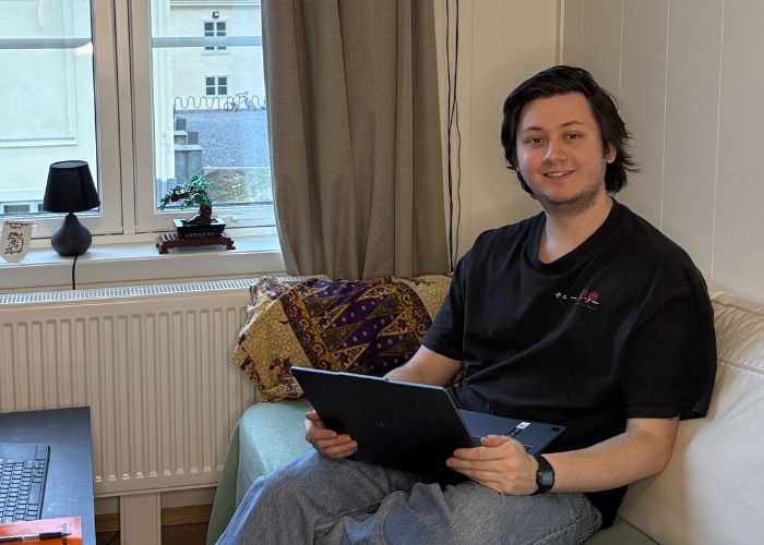 Person sitter i sofaen med en laptop i en hybel med vindu.