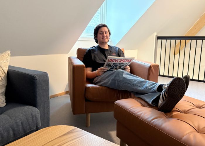 Person som sitter i en stol og holder en avis, med føttene hvilende på en skammel.