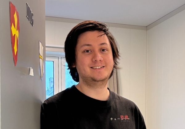 Smilende person som står inntil en dør