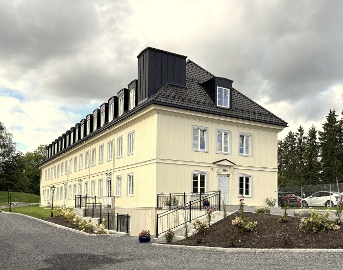 Historisk bygning med moderne elementer, omgitt av grønt landskap og parkeringsplass i forgrunnen.