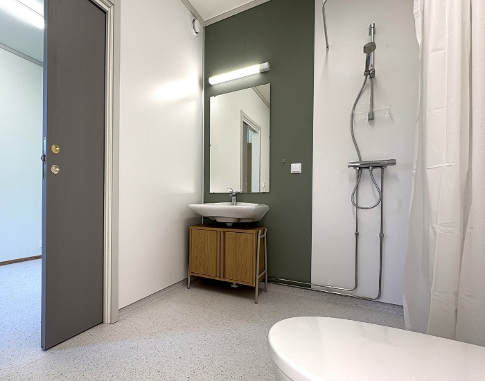 Moderne baderom med dusj, servant og speil, samt åpen dør som gir innsyn til tilstøtende rom. Minimalistisk og funksjonell innredning.