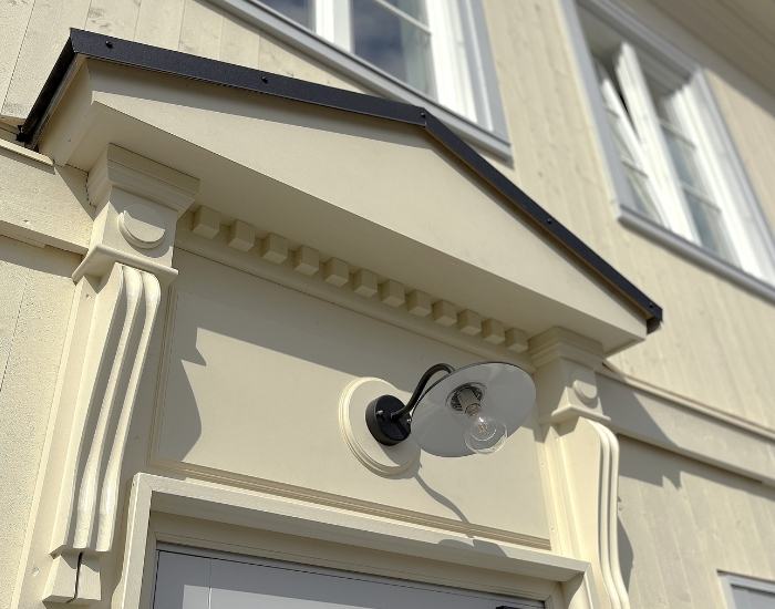 Klassisk inngangsparti med dekorativ utsmykning og utendørs lampe montert på veggen.