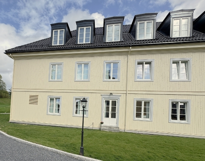 Lys gul trebygning av moduler med svarte arker på taket, omgitt av grønn plen og grussti i forgrunnen.