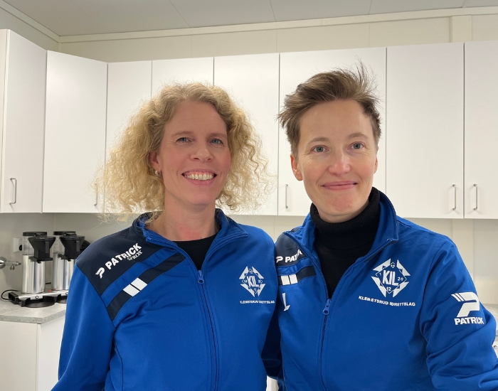 To smilende personer i fotballtrøye står inntil hverandre.