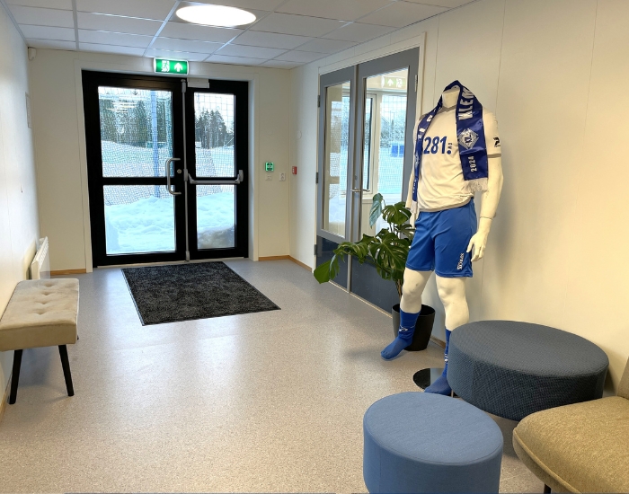 Inngangsparti med sitteplasser og utstillingsdukke med fotballdrakt.