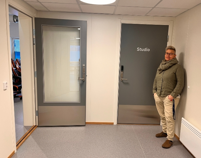 Smilende person som står i hjørnet av en korridor med dører.