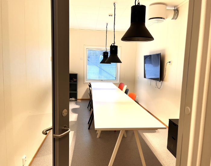 Glassdør som står på gløtt inn mot et lite rom med langbord.