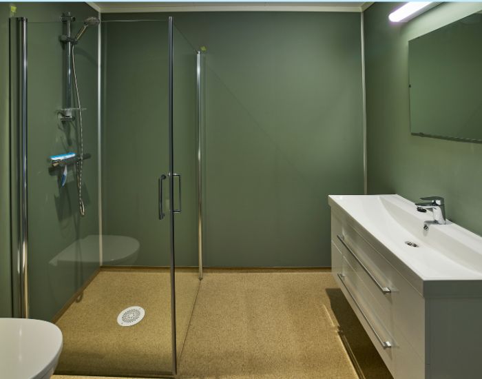 Baderom med perspektiv mot servantmøbel og dusjvegger. Grønne vegger og okergult belegg.
