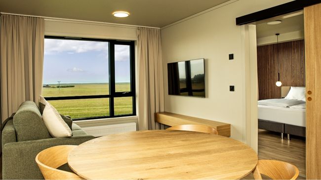 Hotellrom med nordiske møbler. Stort vindu med utsikt mot åpent landskap.