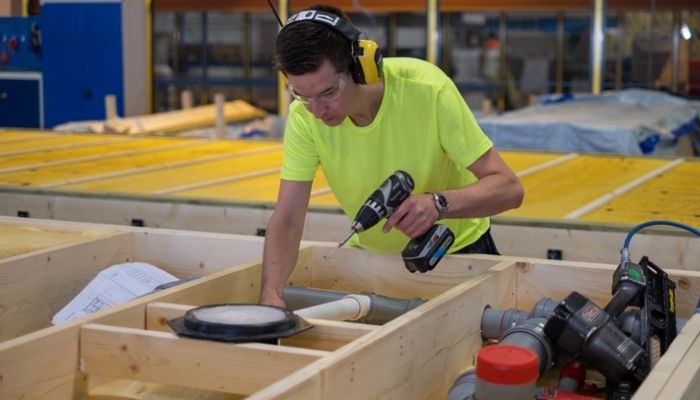 Fabrikkarbeider med Moelven-genser og hørselvern produserer en byggmodul.