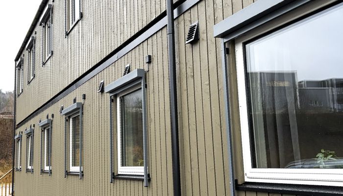 Brungrønt, toestasjes modulbygg med store vinduer og svarte eksteriørdetaljer.