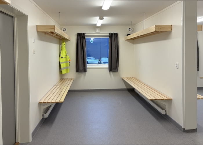 Romslig garderobe i boligrigg med benker og oppheng, tilpasset arbeidsklær og utstyr.