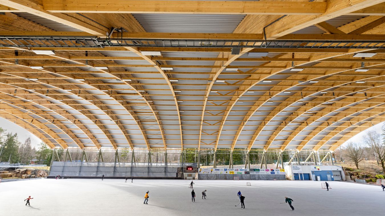 Isbana under tak av limträbalkar, personer som åker på isen