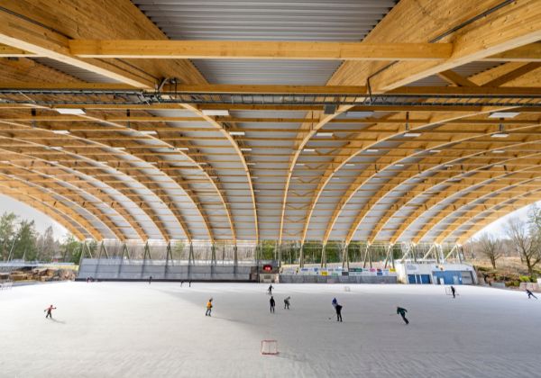 Isbana under tak av limträbalkar, personer som åker på isen