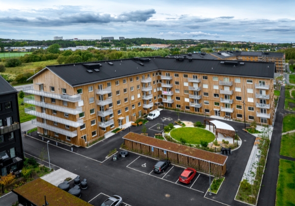 Översiktsbild över bostadshus sett utifrån med träfasad, parkering på innergård