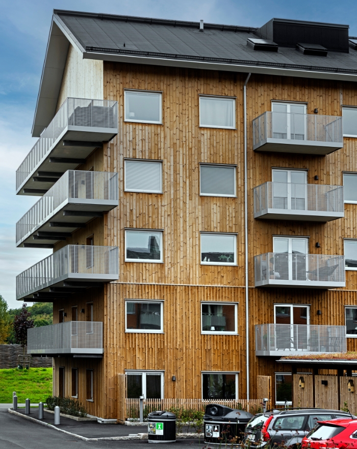 Bostadshus sett utifrån med träfasad och balkonger, bilar står utanför byggnaden.