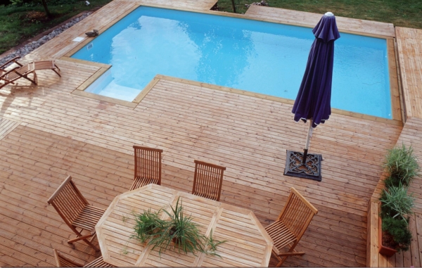 En altan med trall och pool, samt bord, stolar och ett parasoll