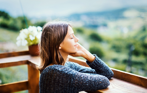 En kvinna lutar sig med sina armbågar mot ett staket , med utsikt mot skogen