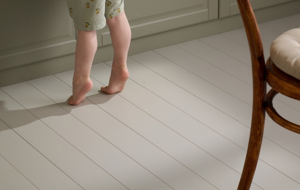 Ett målat trägolv, en stol och ett barns fötter