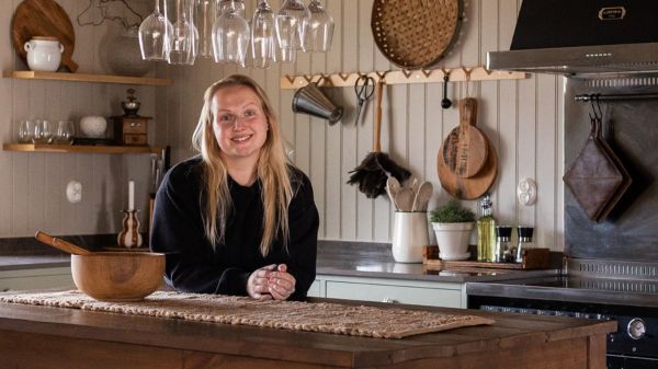 Kvinna lutar sig mot köksön i ett ombonat kök med pärlspont på väggarna