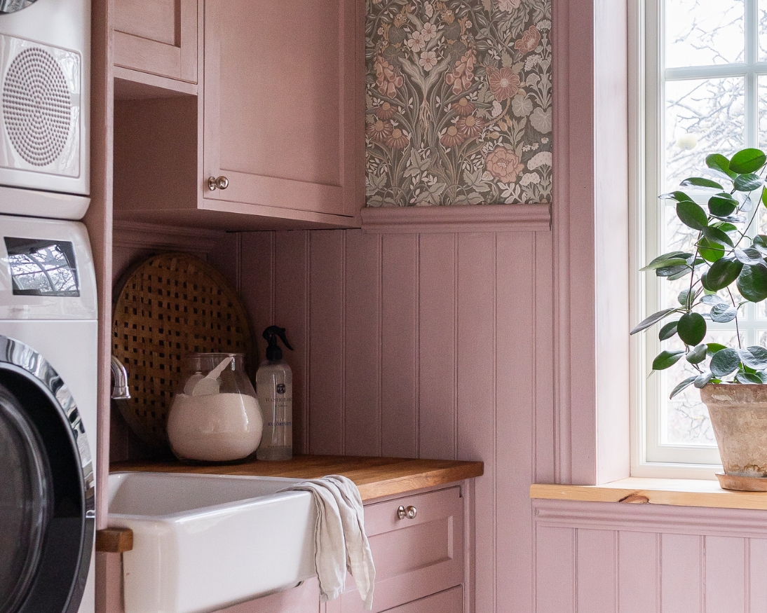 Tvättstuga med rosa bröstpanel, lister och skåp som matchar en blommig tapet.