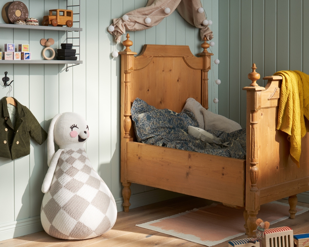 Ett barnrum med en grön träpanel, en säng i trä, en hylla och leksaker