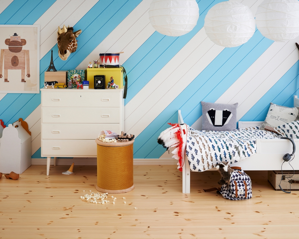 Ett barnrum med blå/vit randig panel på väggen, trägolv, säng, byrå och leksaker