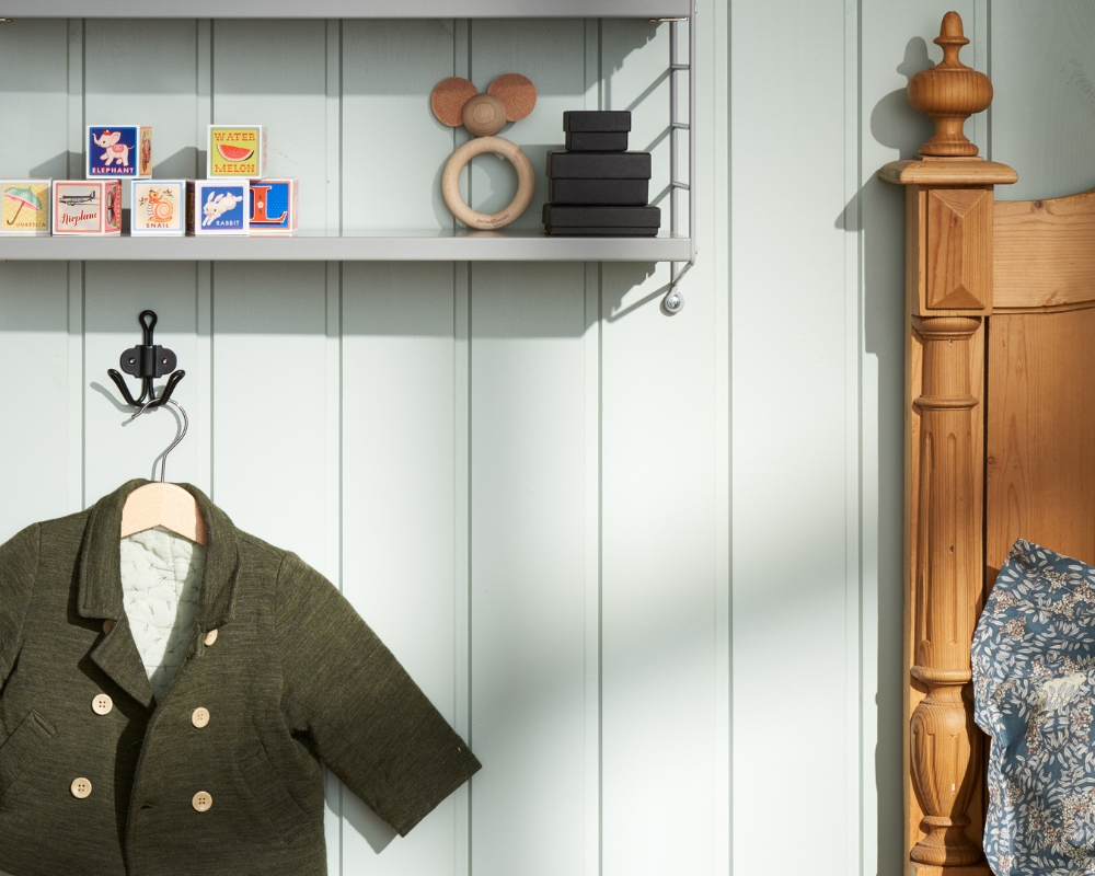 Ett barnrum med grön träpanel på väggarna, en hylla med leksaker, en galge med en kofta, samt en säng i trä
