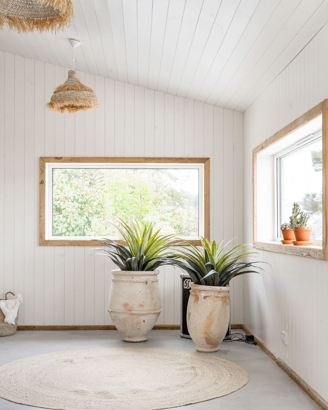 Hörnet på ett rum med stående vit träpanel Trend Slät, två fönster med foder av trä och två stora terrakottakrukor på golvet