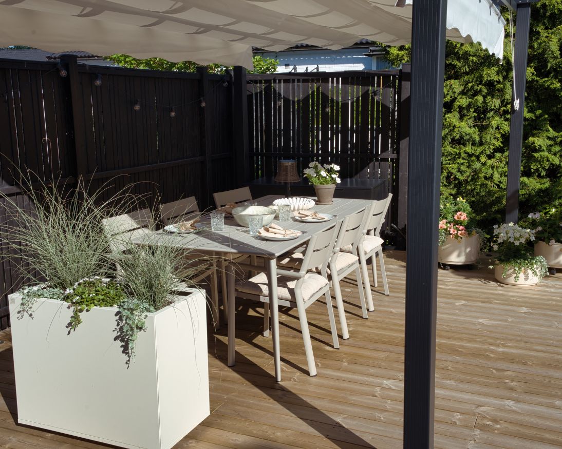 Vit matgrupp under en pergola med vitt tak på en altan 