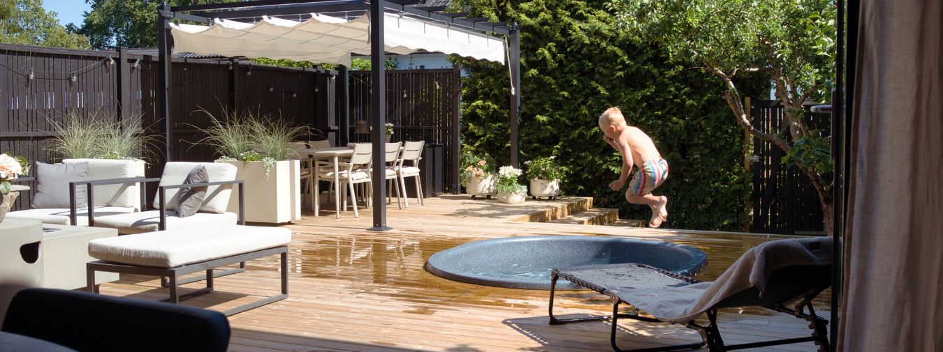 Pojke som hoppar i en rund pool på en altan som är mysigt möblerad